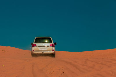 Car on desert against clear blue sky