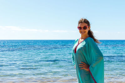 Portrait of smiling young woman standing at beach against sky during summer