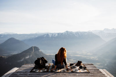 Back view of unrecognizable female tourist sitting at viewpoint in mountains and observing amazing scenery in morning