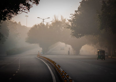 Road by trees against sky in city