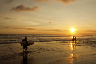Silhouette people walking on beach against sky during sunset