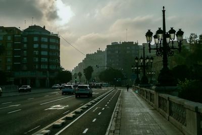 Traffic on road in city against cloudy sky