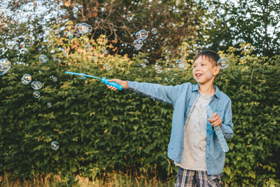 A boy is playing with soap bubbles in a summer park, among the greenery.