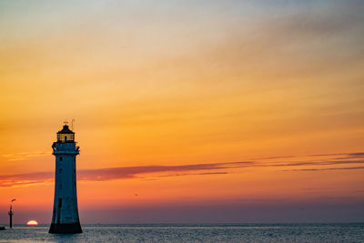 Lighthouse by sea against sky during sunset