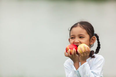 Portrait of cute girl holding apple against white background