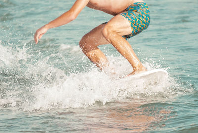 Low section of shirtless man surfing on sea