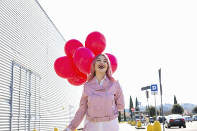 Midsection of woman with pink balloons against sky