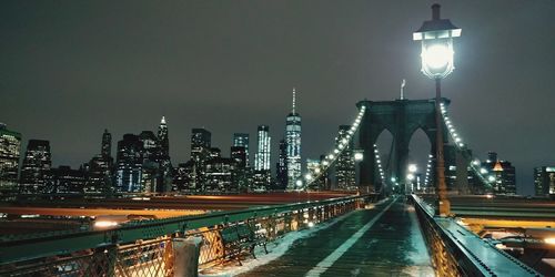 Illuminated brooklyn bridge against buildings at night