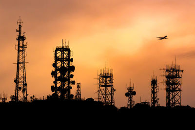 Silhouette telecommunications towers against sky during sunset