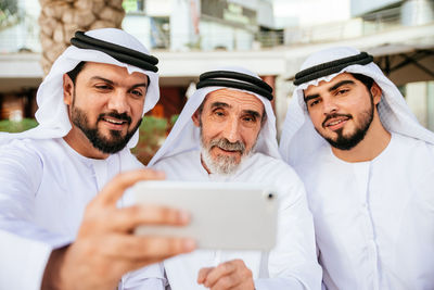 Man with brother and grandfather wearing dish dash taking selfie from phone outdoors