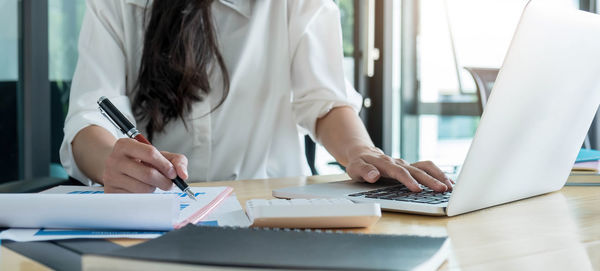 Midsection of woman using mobile phone while sitting on table