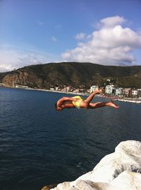 Side view of man jumping in sea against cloudy sky