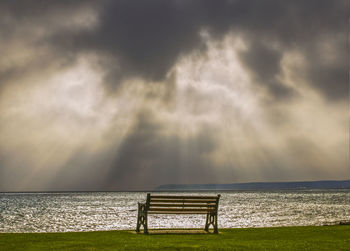 Empty bench on beach against sky