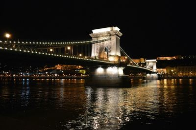 Illuminated bridge over river in city at night