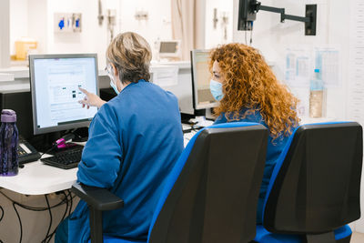 Nurse with colleague discussing over computer at hospital