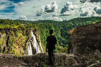 Rear view of man standing on rock against sky