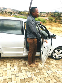 Side view of young man standing by car