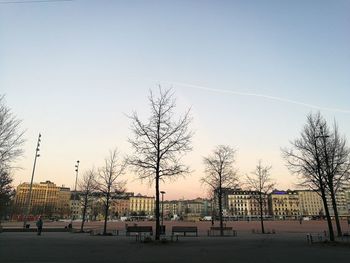 Bare trees by buildings against clear sky during sunset