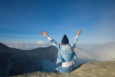 Rear view of woman with arms outstretched sitting on cliff