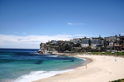 Scenic view of beach by buildings against blue sky