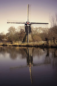 Traditional windmill by lake against clear sky