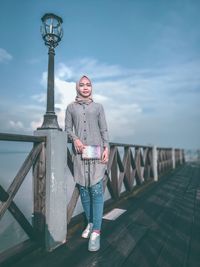 Portrait of woman standing on footbridge in city against sky