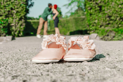 Close-up of baby booties with couple kissing in background at park on sunny day