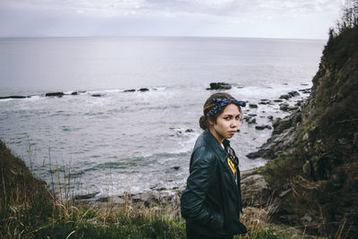 Portrait of confident woman wearing jacket standing against sea