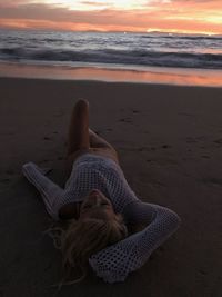 Woman relaxing at beach against sky during sunset