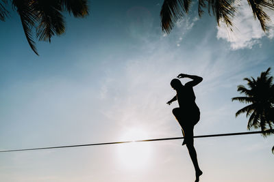 Man slacklining on rope against sky during sunset