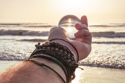 Midsection of man holding sunglasses at beach against sky