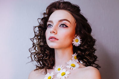 Close-up of beautiful young woman wearing flowers and make-up against wall