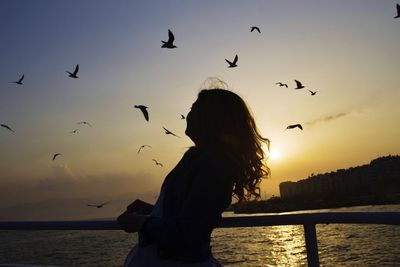 Silhouette woman standing by sea against sky during sunset