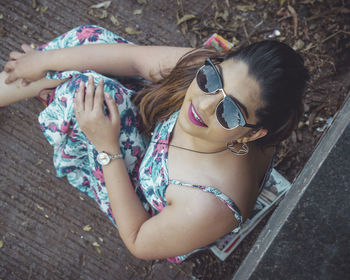 High angle portrait of beautiful woman wearing sunglasses sitting outdoors