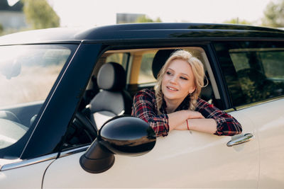 Portrait of a smiling young woman sitting on car