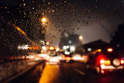 Illuminated city seen through wet window during rainy season