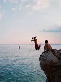 Rear view of man jumping from cliff against sky