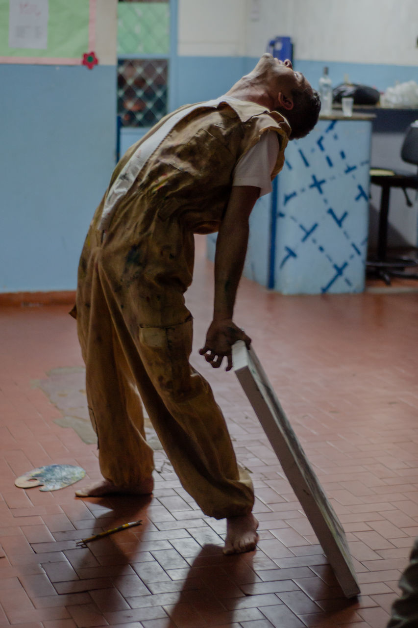 indoors, flooring, one person, full length, art and craft, creativity, representation, real people, men, side view, occupation, craft, human representation, skill, lifestyles, arts culture and entertainment, bending, focus on foreground, clothing, tiled floor