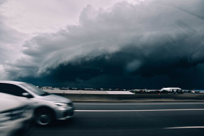 Vehicles on road against cloudy sky