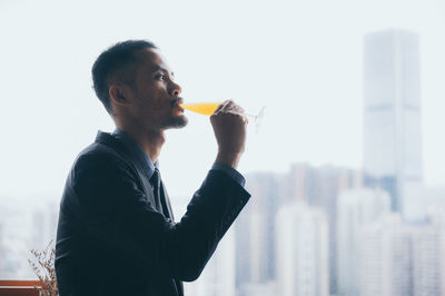 Young man drinking glass against cityscape