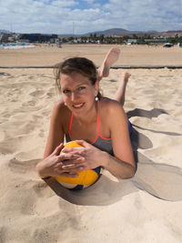 Portrait of young woman holding ball on beach