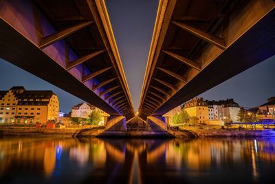 Illuminated bridge over river by buildings against sky at night