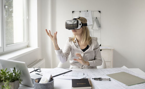 Businesswoman gesturing while wearing virtual reality simulator by laptop on table