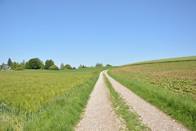 Dirt road amidst field against clear blue sky