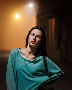 Portrait of young woman standing on road in city at night