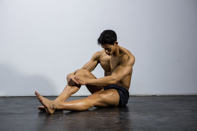 Shirtless muscular man sitting against wall