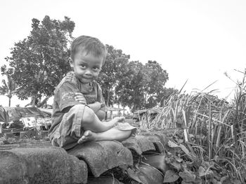 Cute boy sitting on plant against clear sky