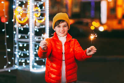 A charming boy holds a sparkler in his hands, celebrating the new year at night on the street. 