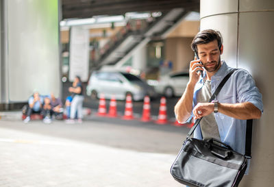 A young caucasian man watching the time and calling on his cell phone while waiting for his friend.