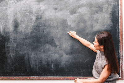 Side view of teacher writing on blackboard in classroom
